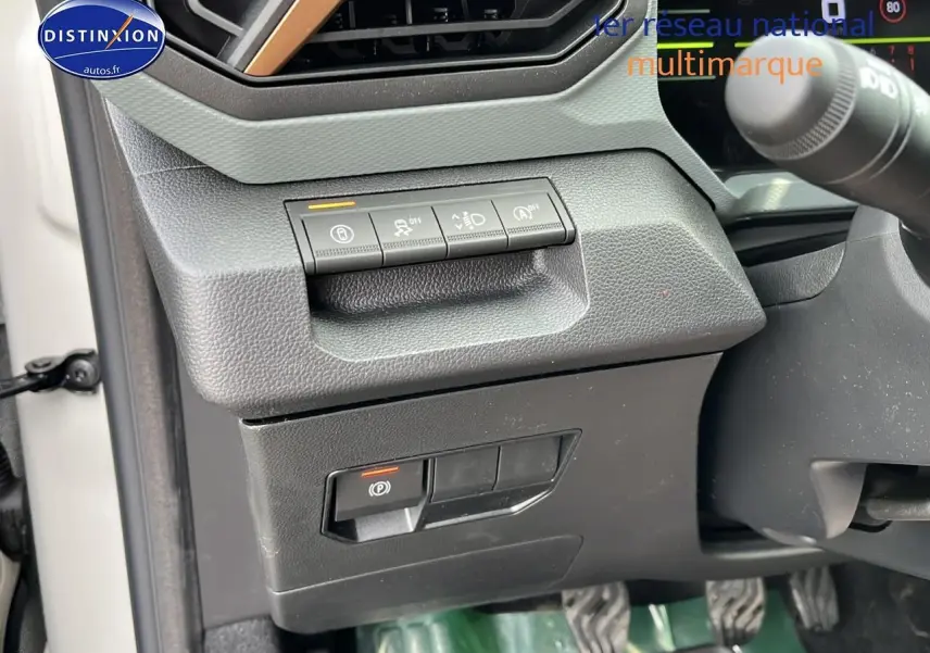 Détail des commandes côté gauche du tableau de bord du Dacia Duster Sandstone 2025, avec boutons d'assistance et frein à main électrique.