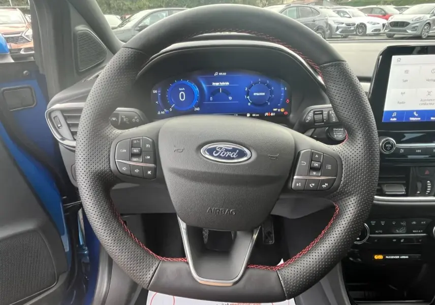 Vue intérieure centrée sur le volant perforé avec surpiqûres rouges du Ford Puma bleu 2022, tableau de bord numérique visible.