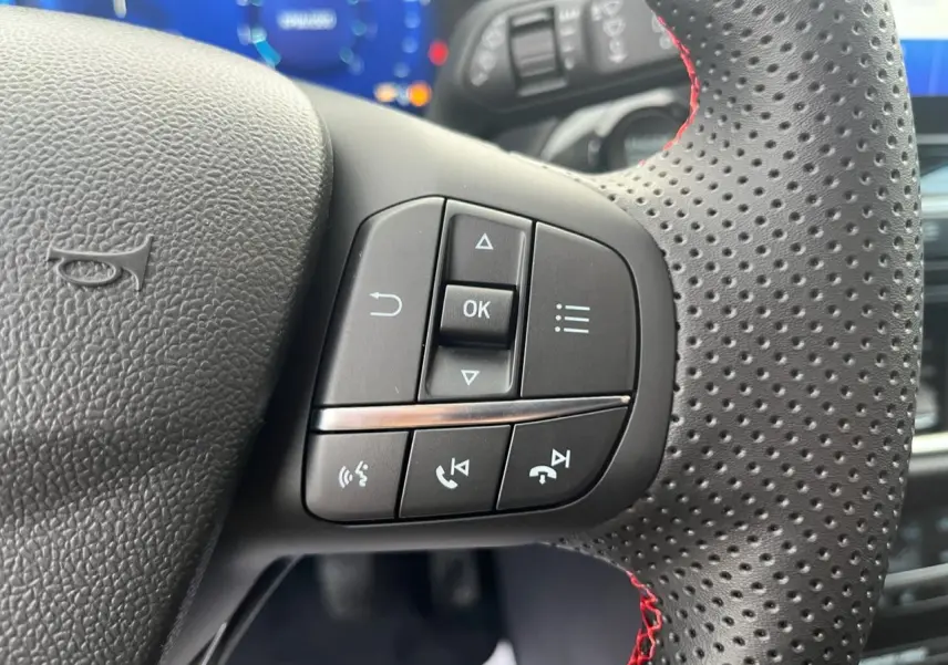 Gros plan sur les commandes multifonctions du volant perforé avec surpiqûres rouges d'un Ford Puma bleu 2022.