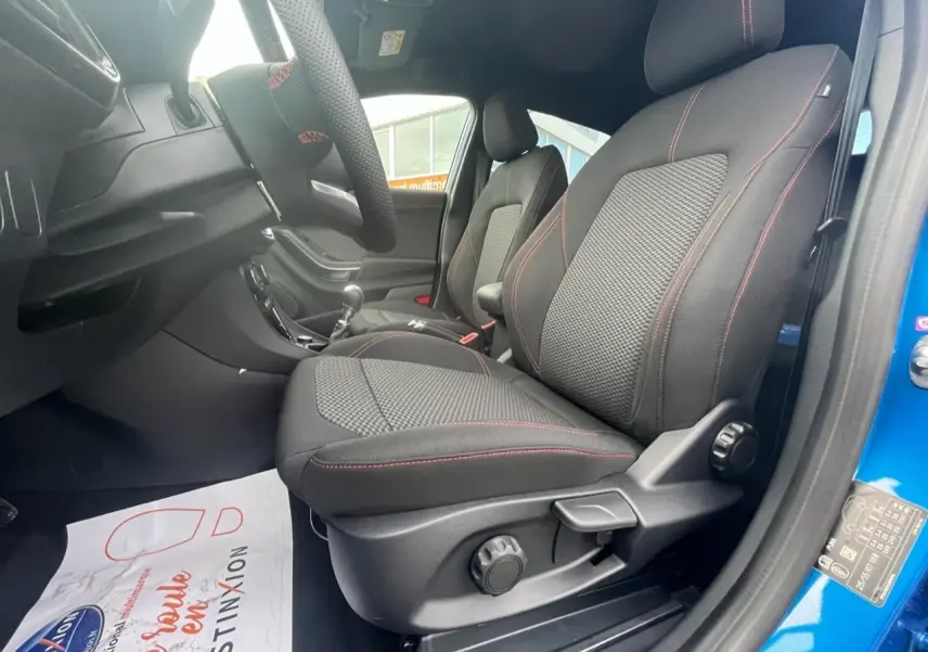 Intérieur du Ford Puma 2022 bleu, vue côté droit sur sièges avant noirs avec surpiqûres rouges et volant.