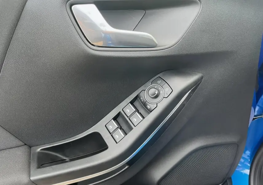 Gros plan sur la porte côté conducteur du Ford Puma bleu, montrant les commandes électriques des vitres et le bouton de réglage des rétroviseurs.