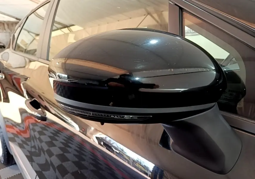 Gros plan sur le rétroviseur côté gauche noir brillant d’un Renault Captur Business 2021, avec reflet de l’environnement.