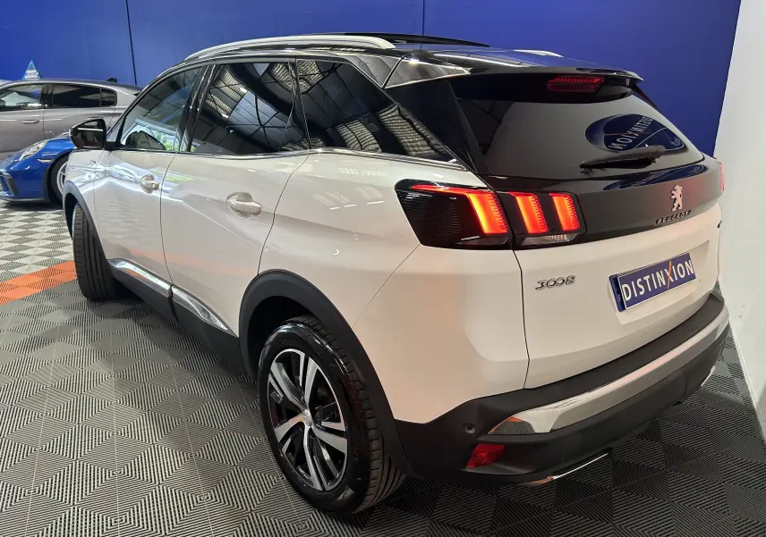 Vue 3/4 arrière droite d’un Peugeot 3008 blanc avec feux arrière allumés et toit ouvrant en intérieur showroom.