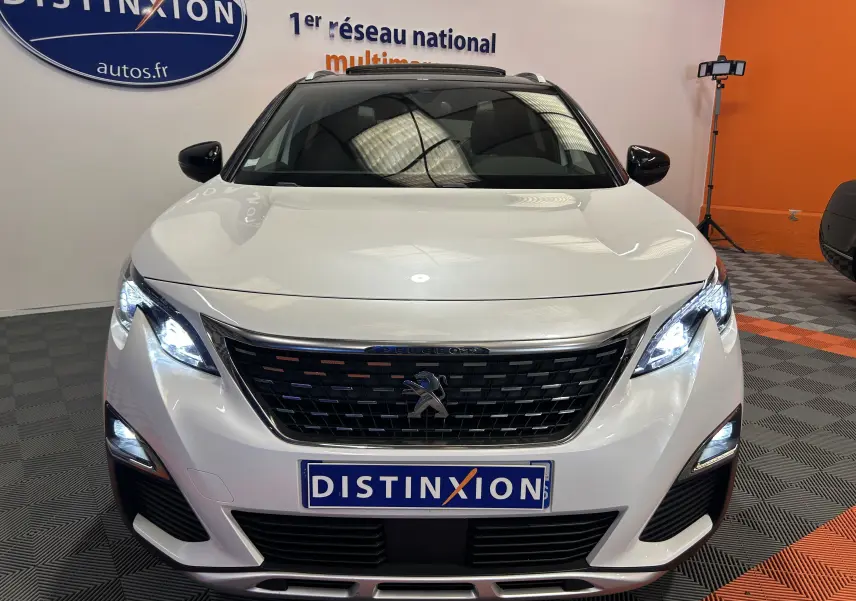 Vue de face d'un Peugeot 3008 blanc avec calandre noire et phares LED allumés dans un showroom.