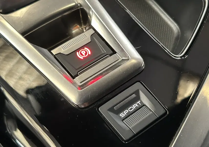 Gros plan sur la console centrale noire du Peugeot 3008 avec bouton frein à main électronique et mode Sport.