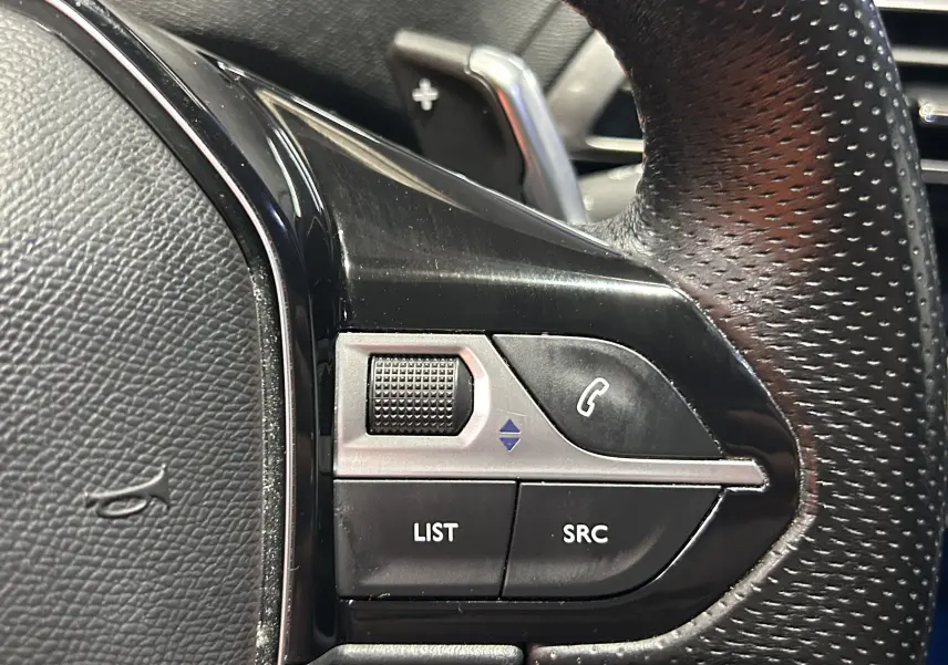 Gros plan sur les commandes gauche du volant perforé du Peugeot 3008 blanc, avec molette et boutons fonction audio.