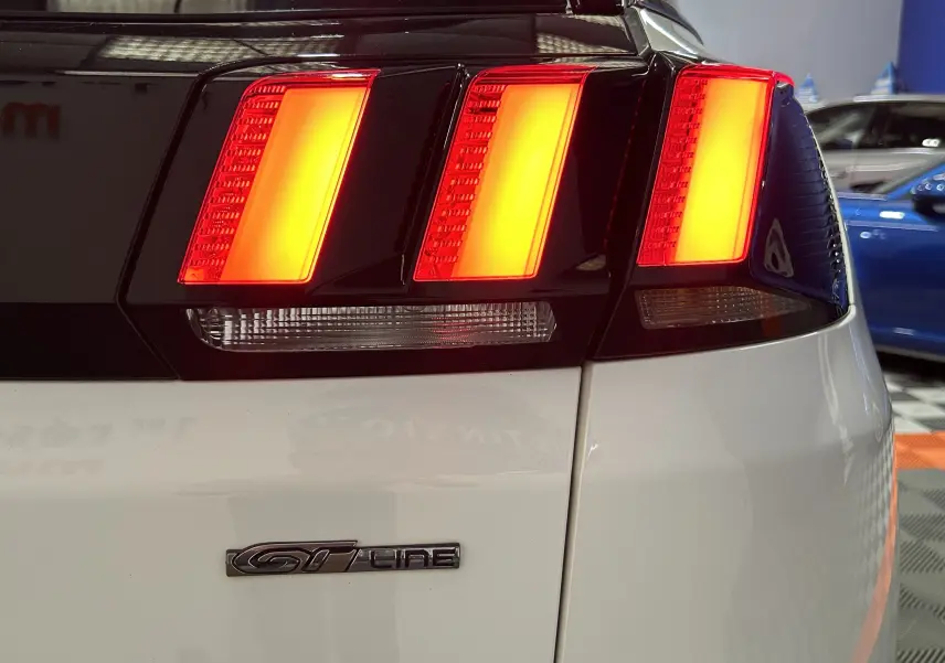 Gros plan sur le feu arrière droit allumé et le badge GT Line d’un Peugeot 3008 blanc, vue arrière partielle.