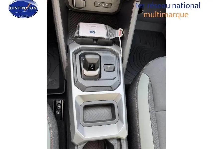 Vue plongeante sur la console centrale du Dacia Duster 2025, avec levier de vitesses et accoudoir entre sièges noirs.