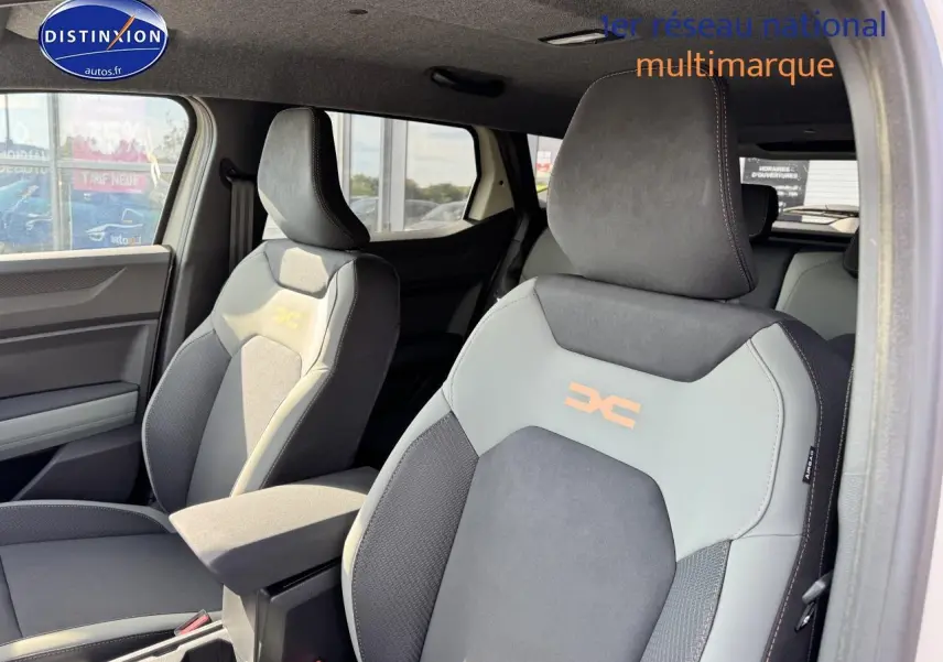 Vue intérieure des sièges avant gris et noir du Dacia Duster 2025 avec accoudoir central et logo distinctif brodé.