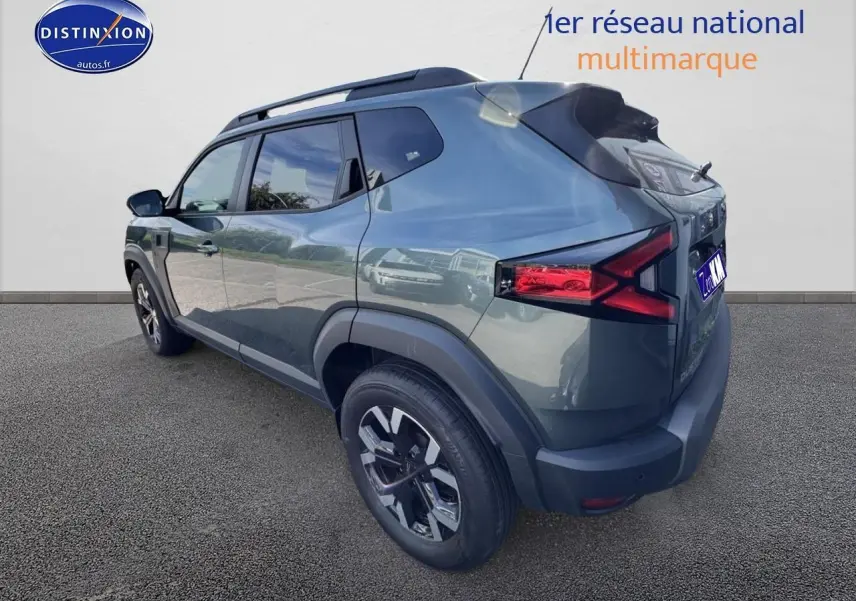 Vue 3/4 arrière droite d'un Dacia Duster 2025 vert cèdre avec barres de toit et jantes alu noires.