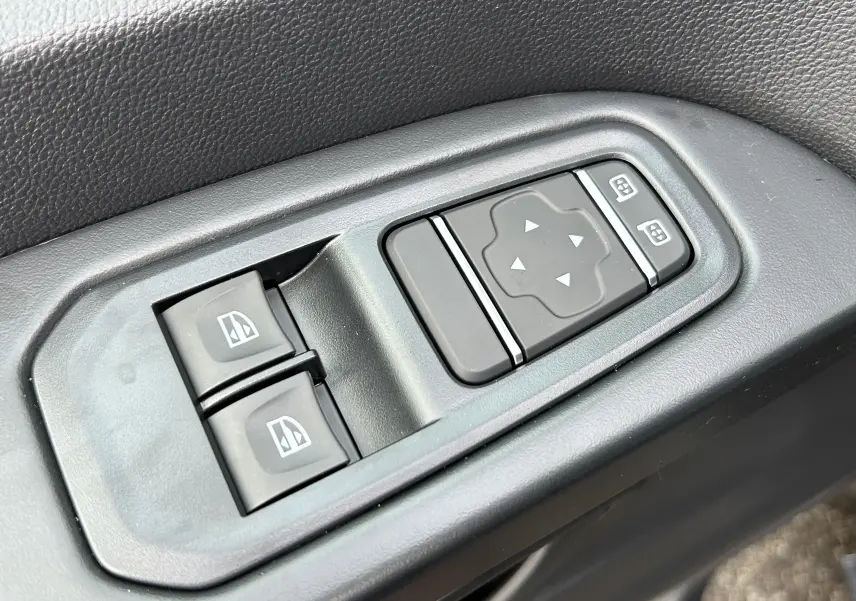 Gros plan sur les commandes de réglage des vitres et des rétroviseurs du Renault Trafic Fourgon gris Comète, côté conducteur.