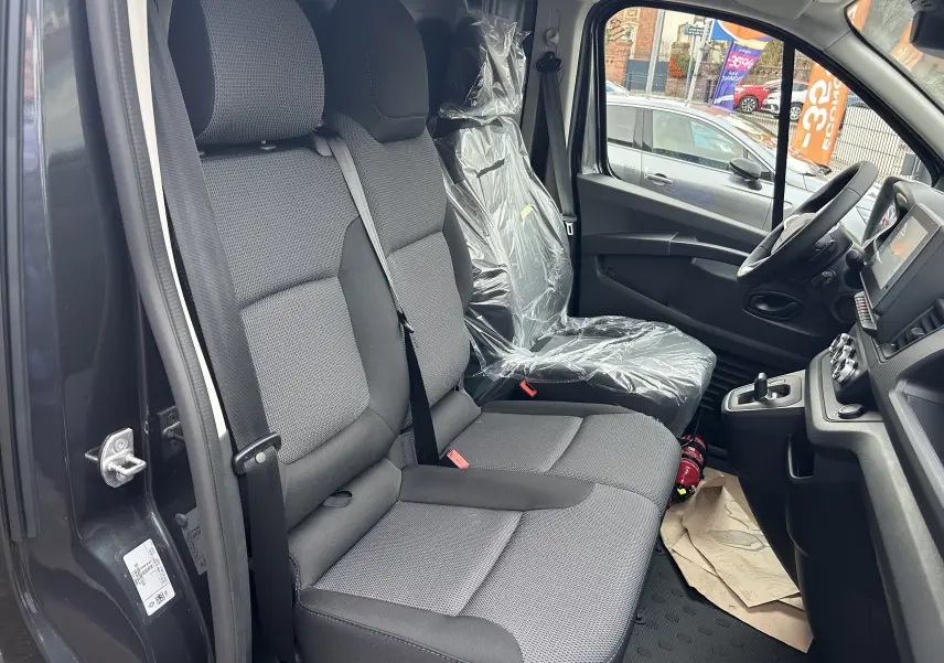 Vue intérieure côté conducteur du Renault Trafic Fourgon gris Comète, montrant les sièges avant et le tableau de bord.