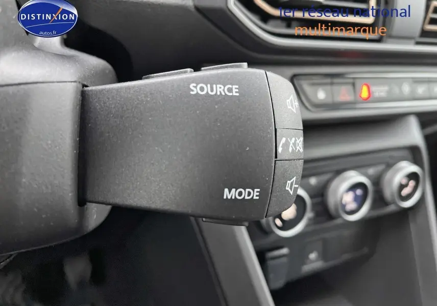 Gros plan sur la commande audio au volant du Dacia Jogger blanc, avec tableau de bord et commandes clim visibles en arrière-plan.