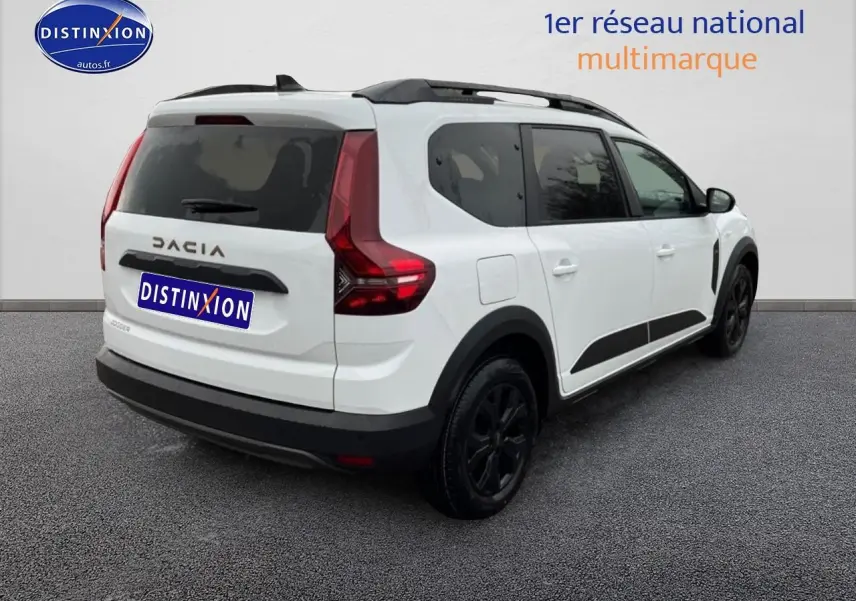 Vue 3/4 arrière droite d'un Dacia Jogger blanc avec barres de toit noires et vitres arrière surteintées.