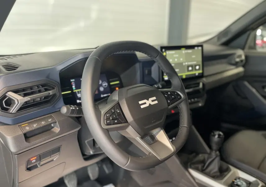 Vue intérieure du poste de conduite du Dacia Duster 2025, volant multifonction noir et écran tactile central visible.