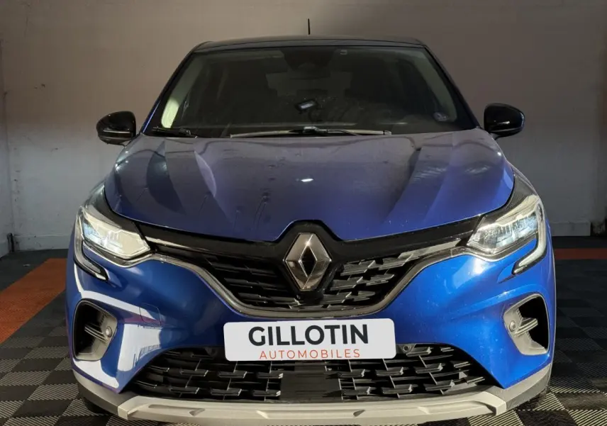 Vue avant d'un Renault Captur bleu 2024 avec calandre noire et phares LED allumés dans un garage.