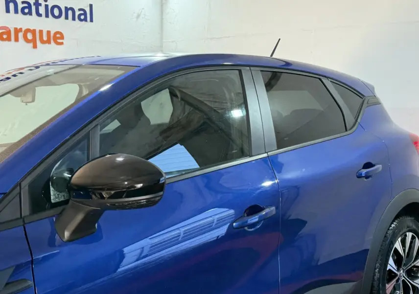 Vue latérale gauche du Renault Captur bleu 2024 avec rétroviseur noir brillant et vitres teintées.