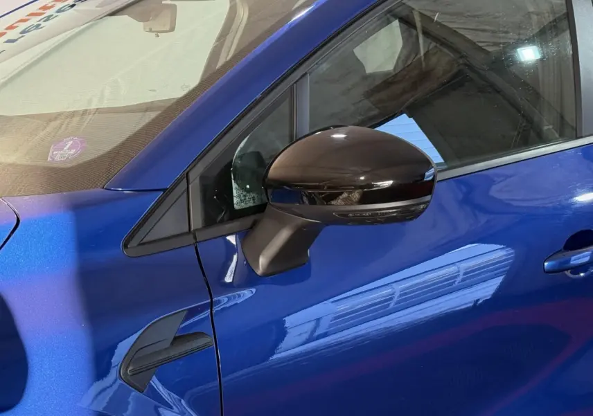 Détail du côté gauche d’un Renault Captur bleu 2024 avec rétroviseur noir brillant et poignée de porte visible.