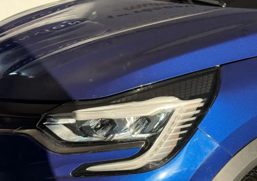 Gros plan sur le phare avant droit du Renault Captur bleu 2024 avec détails LED et carrosserie métallisée.