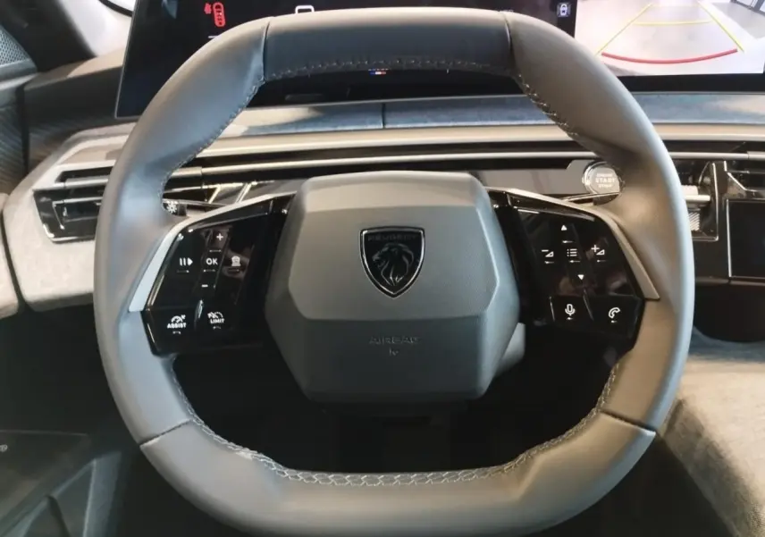Vue rapprochée du volant gris du Peugeot 3008 2025 avec commandes intégrées et écran incurvé flottant en arrière-plan.