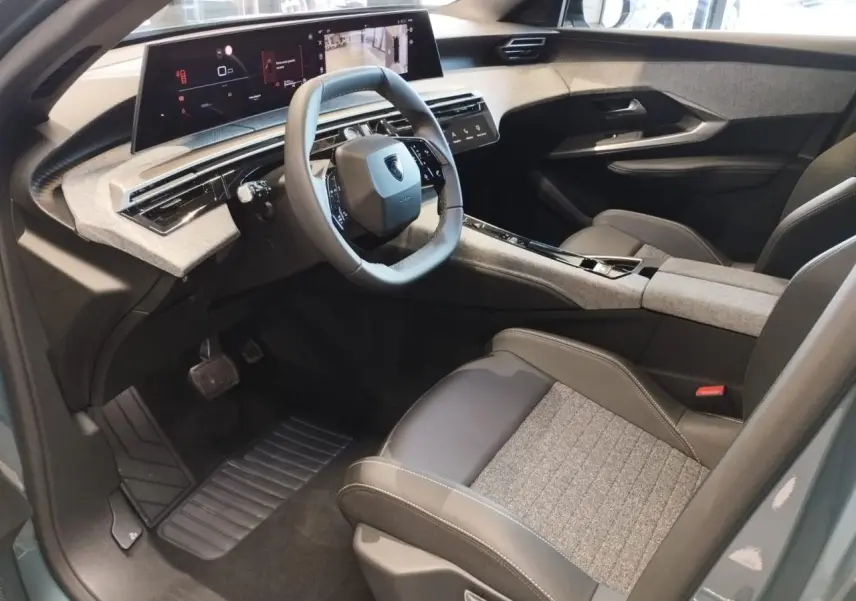 Vue intérieure côté conducteur du Peugeot 3008 Hybrid 2025 avec tableau de bord et écran incurvé, sellerie tissu gris et cuir noir.