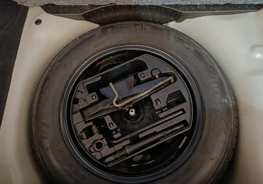 Vue rapprochée de la roue de secours et des outils de bord dans le coffre d'une Citroën C3 blanche de 2020.