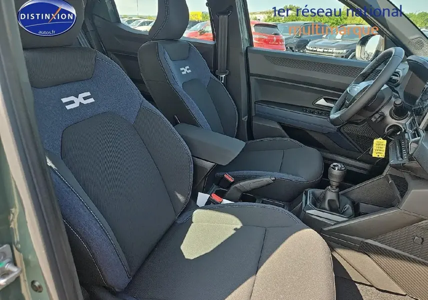 Intérieur avant du Dacia Duster 2025 vert kaki, sièges tissu noir et bleu avec accoudoir central et boîte manuelle visible