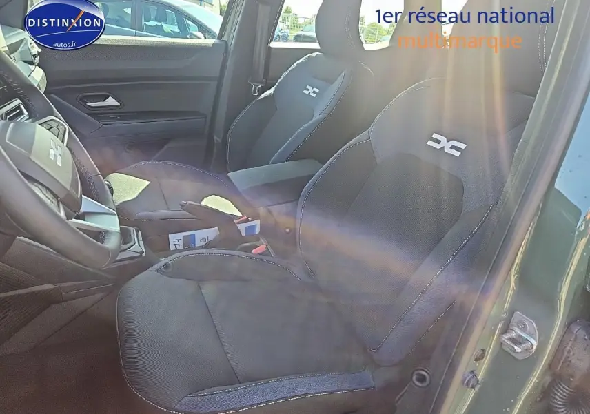 Intérieur du Dacia Duster 2025 vert kaki, vue côté droit sur sièges avant avec logo DC brodé et accoudoir central.
