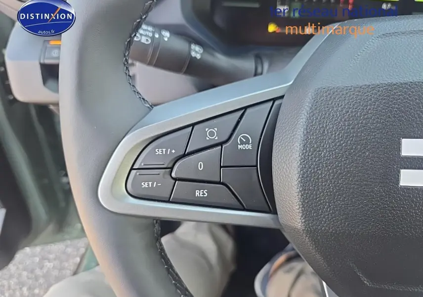 Gros plan sur les commandes à gauche du volant du Dacia Duster vert kaki 2025, montrant les boutons de régulateur de vitesse.