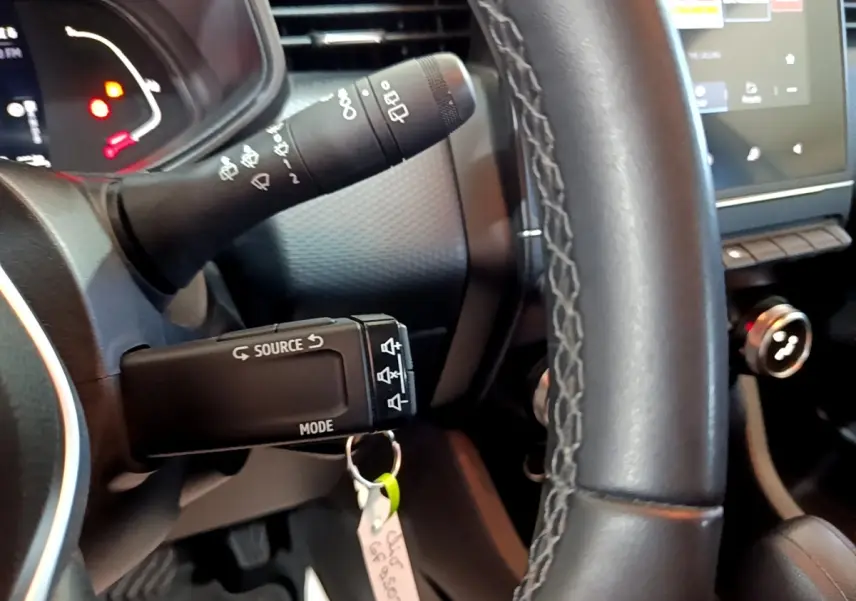 Gros plan sur le volant cuir et les commandes au volant d'une Renault Clio Business E-TECH 140 gris foncé, tableau de bord en arrière-plan.