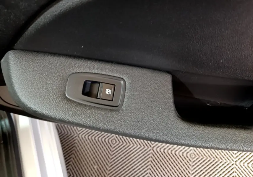 Détail de l'interrupteur de lève-vitre arrière sur la porte intérieure noire d'une Renault Clio Business E-TECH 140 gris foncé.