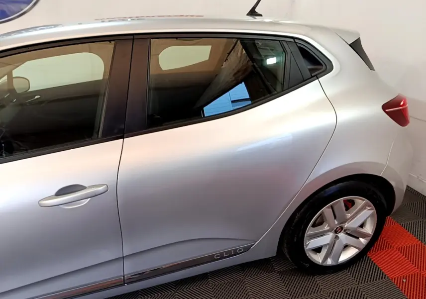 Vue latérale droite d'une Renault Clio gris clair avec jantes alliage et logo Clio sur la porte arrière.