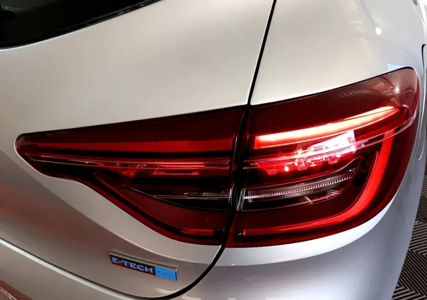 Gros plan sur le feu arrière droit rouge et le badge E-TECH sur la carrosserie gris clair d'une Renault Clio.
