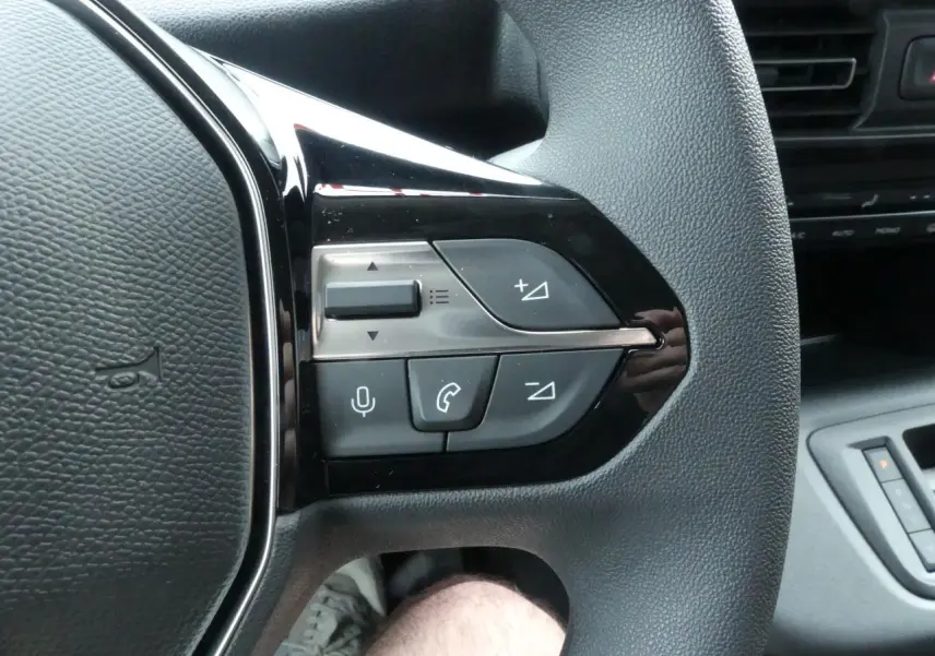 Gros plan sur les commandes multifonctions côté gauche du volant du Peugeot Partner blanc, intérieur cabine visible en arrière-plan.
