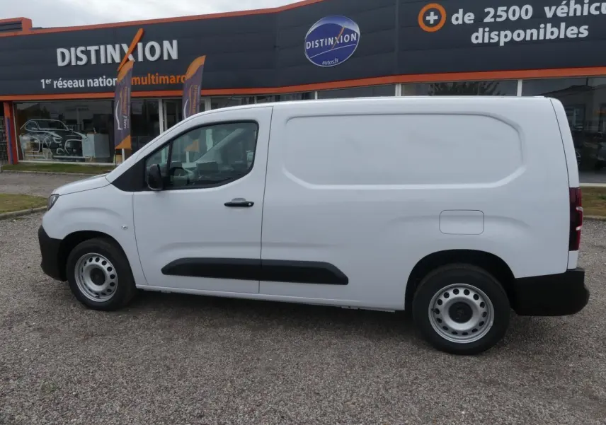Vue de profil côté gauche d’un utilitaire Peugeot Partner blanc avec jantes tôles et protections noires sur porte latérale coulissante.
