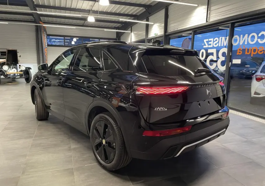 Vue 3/4 arrière droite du DS7 Crossback noir métallisé avec feux arrière DS Pixel LED allumés en intérieur showroom.