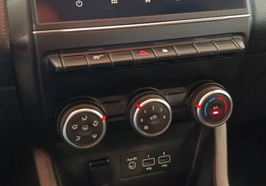 Gros plan sur la console centrale de la Renault Clio Business blanche, montrant les commandes de climatisation et les ports USB.