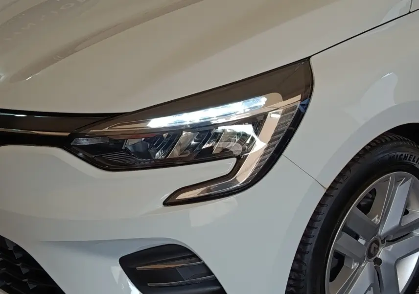 Gros plan sur l'avant droit blanc de la Renault Clio 2021, mettant en valeur le phare LED et la jante alliage.