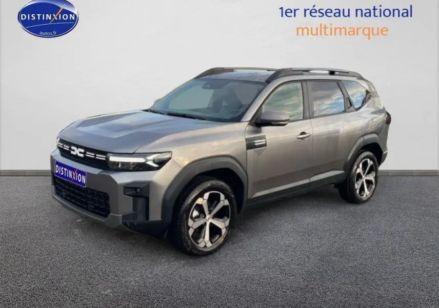 Vue 3/4 avant d'un Dacia Bigster gris schiste métal avec jantes alliage et barres de toit noires.