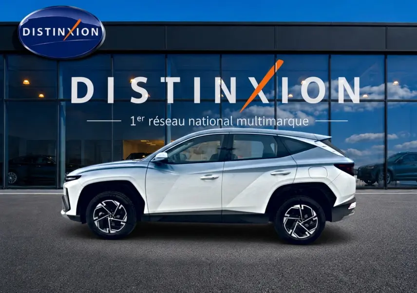Vue de profil côté gauche d'un Hyundai Tucson blanc 2026 hybride devant une vitrine Distinxion.