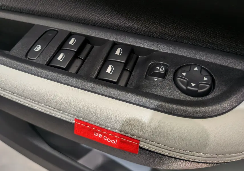 Gros plan sur les commandes de vitres et rétroviseurs côté gauche du Citroën C3 Aircross Hybride 2025 avec étiquette rouge "be cool".
