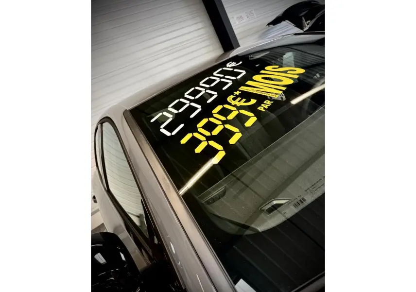 Vue partielle en plongée sur l'avant gauche d'une Peugeot 308 gris selenium avec prix affiché sur le pare-brise.