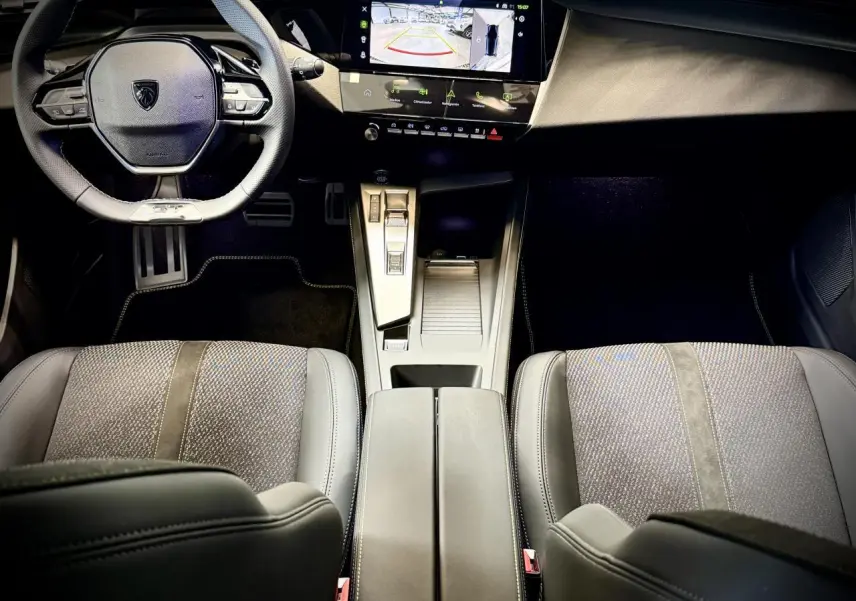 Vue intérieure avant de la Peugeot 308 GT 2025, montrant le volant cuir, la console centrale et les sièges tissu/TEP gris.