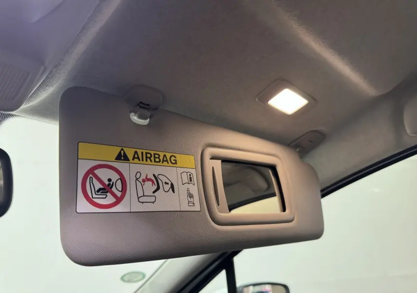 Vue intérieure rapprochée du pare-soleil côté conducteur beige avec miroir et avertissement airbag dans une Renault ZOE blanche 2020.