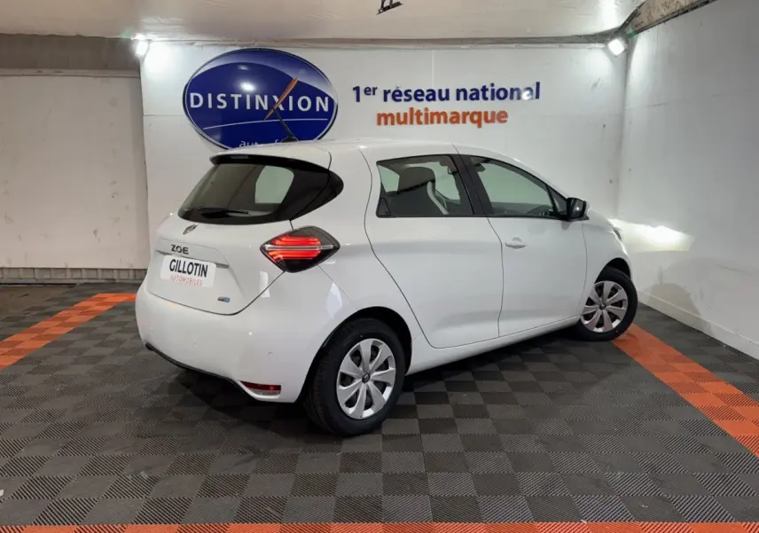 Renault ZOE blanche vue 3/4 arrière droit en intérieur, feux arrière LED et jantes acier avec enjoliveurs.