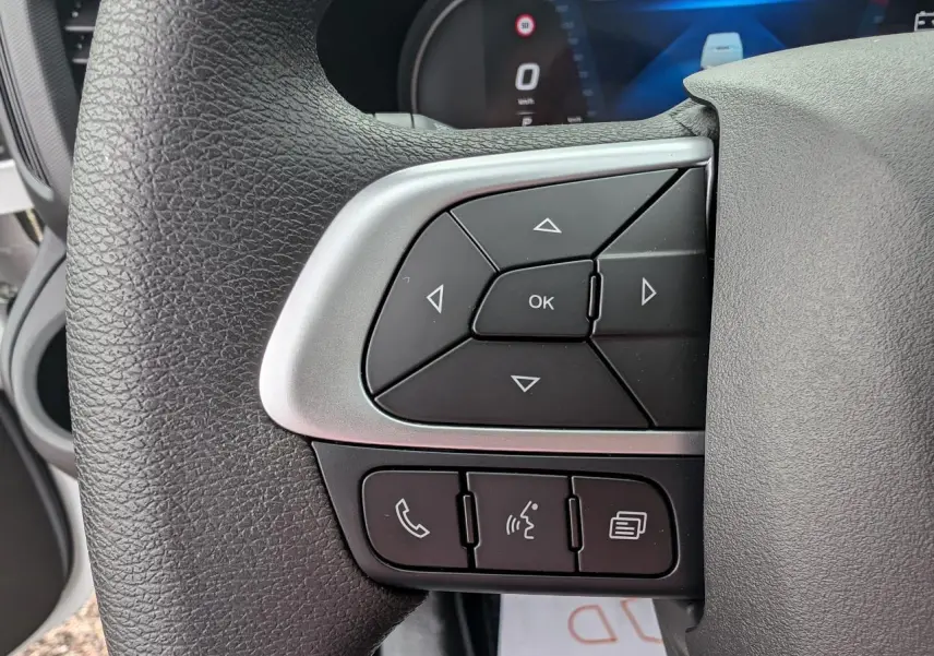 Gros plan sur les commandes multifonctions du volant noir de l’IVECO Daily 35S16 blanc, affichage digital en arrière-plan.