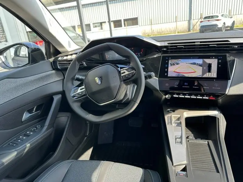 Vue intérieure côté conducteur de la Peugeot 308 2025, tableau de bord noir avec écran tactile et caméra de recul affichée.
