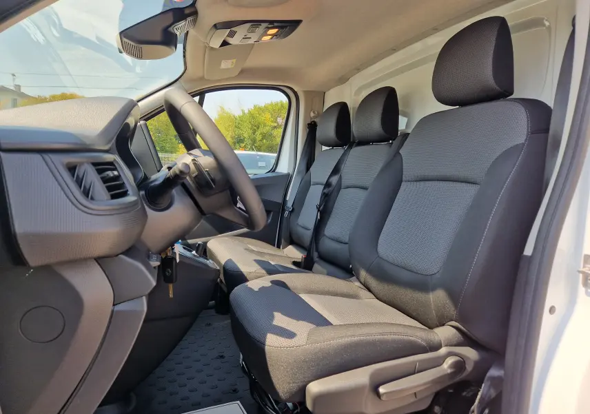 Vue intérieure côté conducteur du Renault Trafic Fourgon blanc 2026, montrant les sièges avant en tissu gris et tableau de bord.