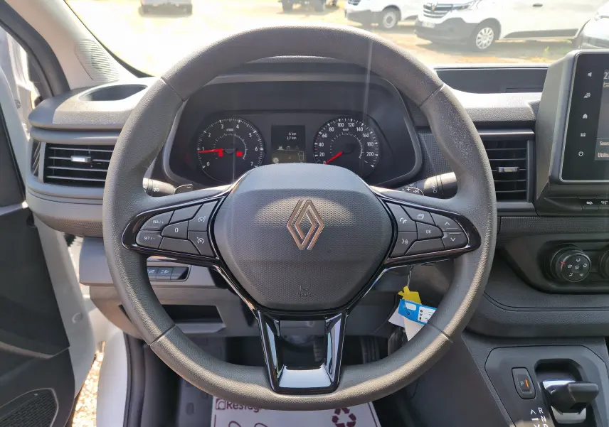 Vue intérieure centrée sur le volant noir du Renault Trafic Fourgon blanc, avec tableau de bord et écran tactile visible.