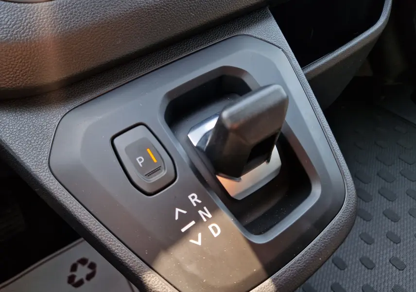 Gros plan sur le levier de vitesses automatique noir du Renault Trafic blanc, avec bouton parking éclairé en orange.